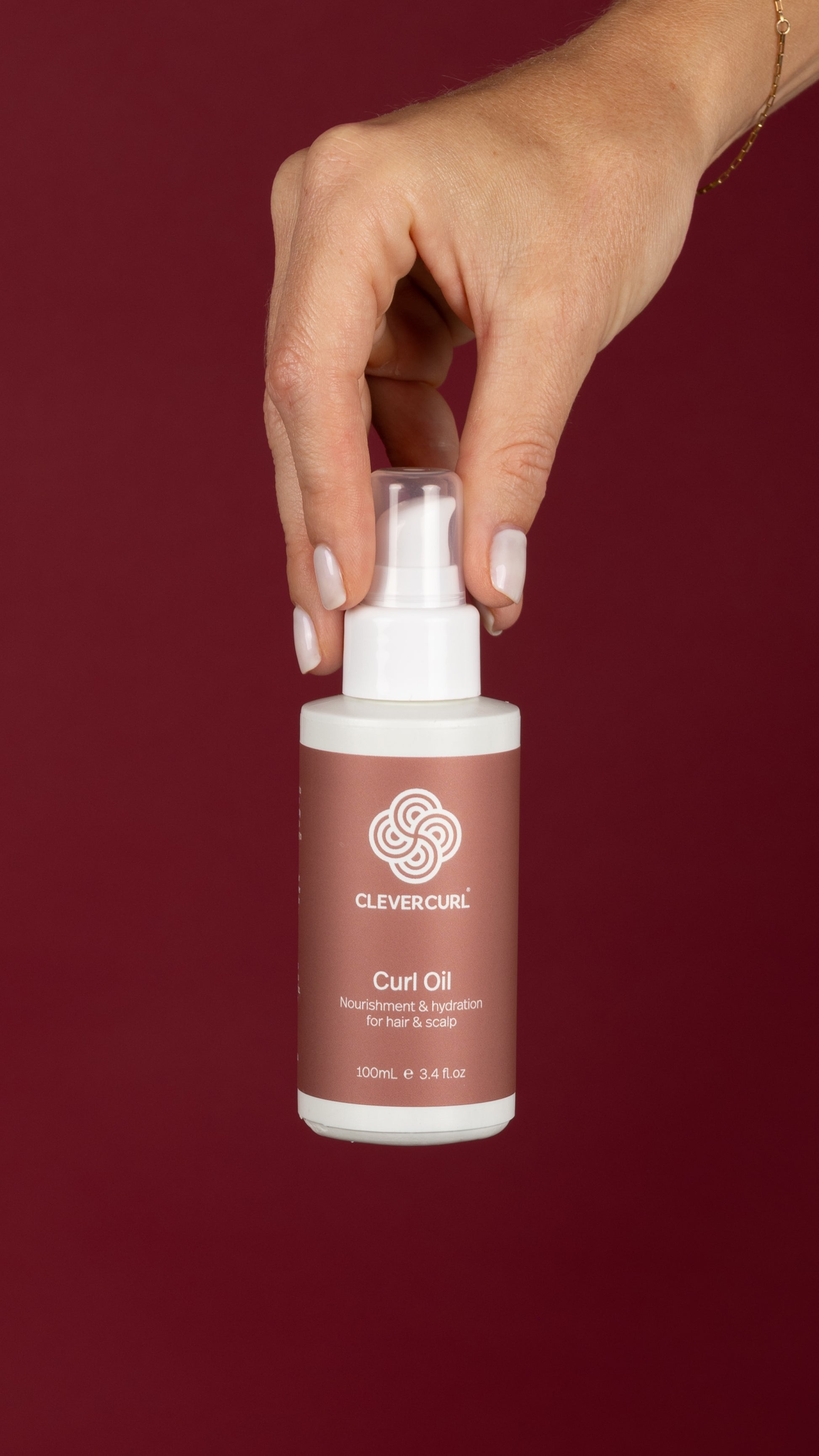 Hand holding a bottle of Clever Curl Curl Oil against a red background